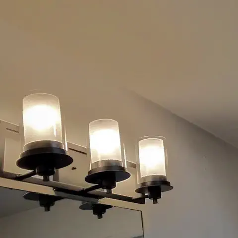 A new three-light fixture, lit, over a bathroom vanity mirror